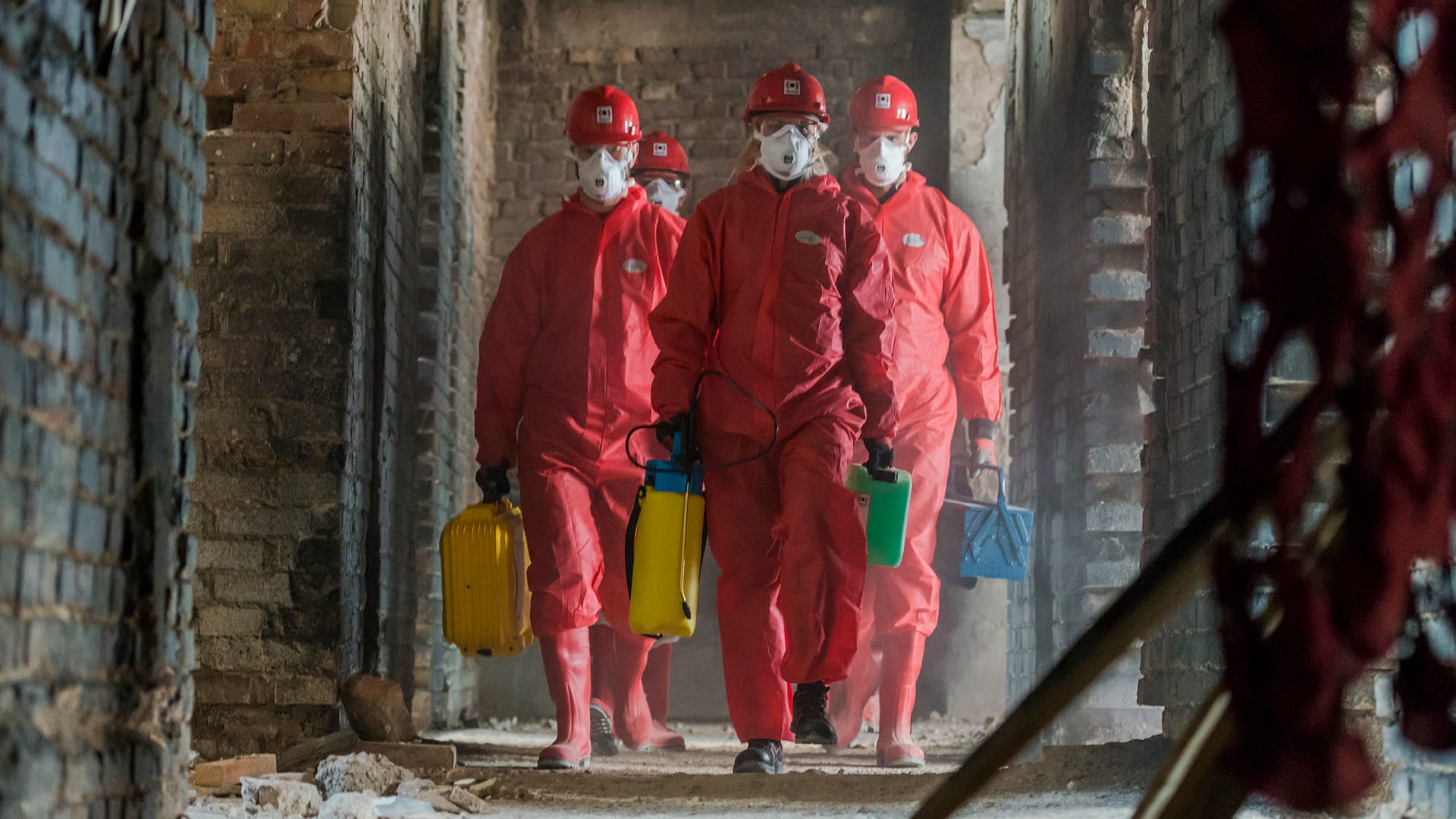 Männliche Mitarbeiter in roten PSA-Anzügen, die in einem beschädigten Gebäude gehen