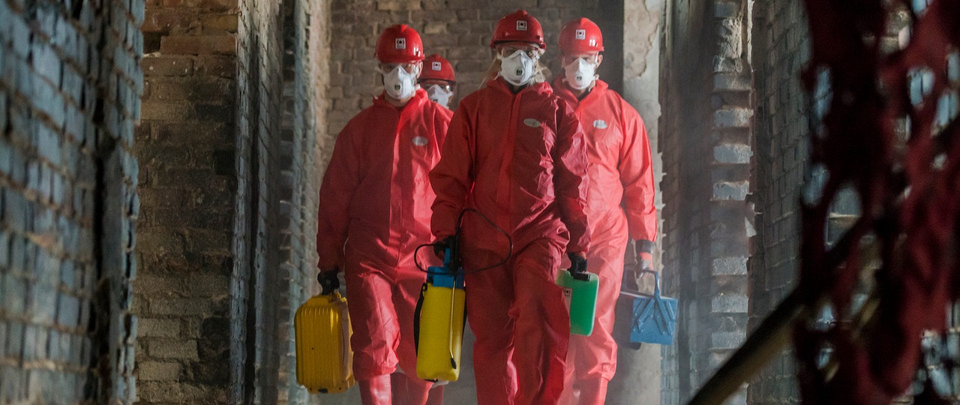 Männliche Mitarbeiter in roten PSA-Anzügen, die in einem beschädigten Gebäude gehen