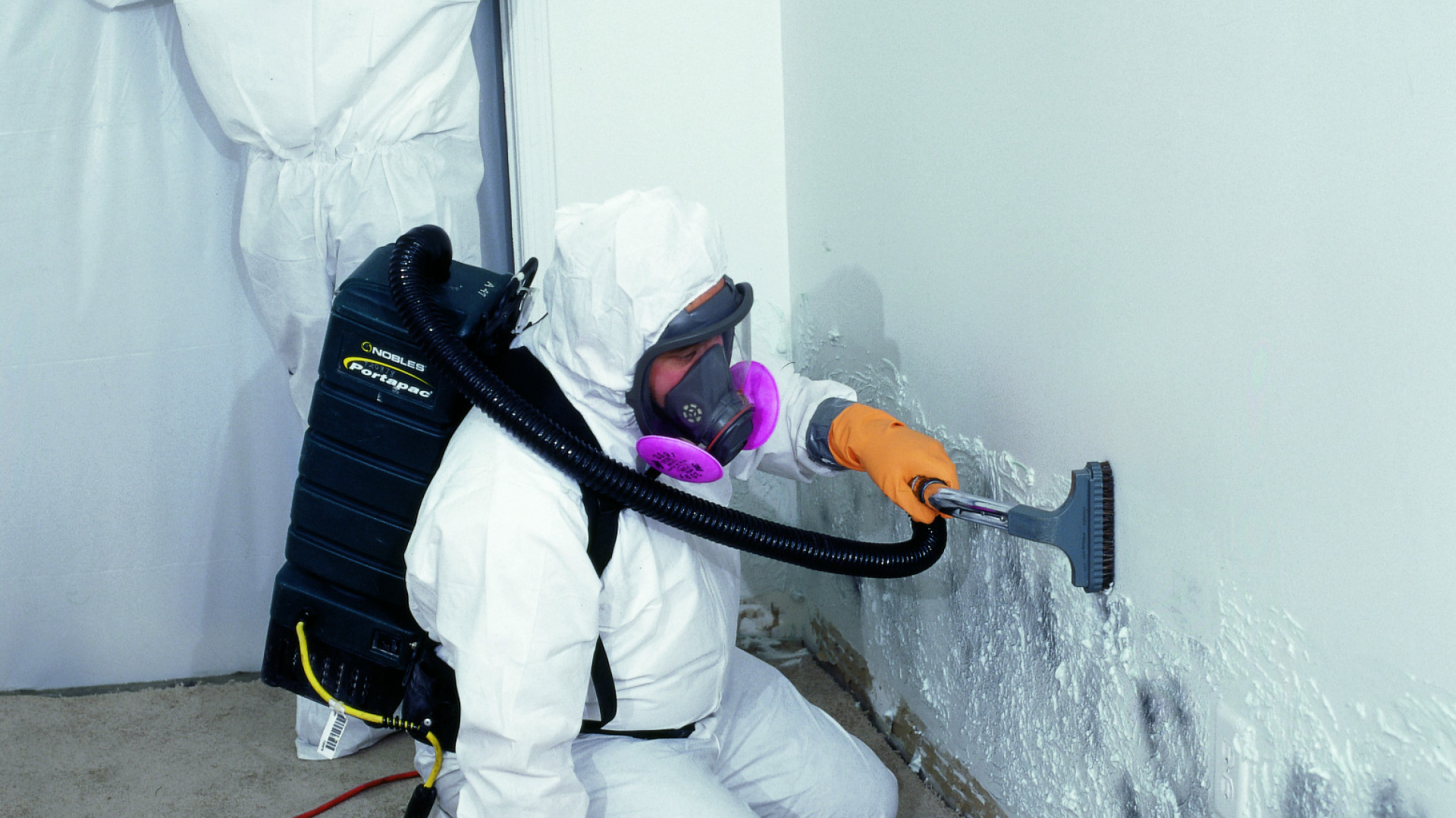 Un ouvrier portant un équipement de protection individuelle et enlevant les contaminants d'un mur