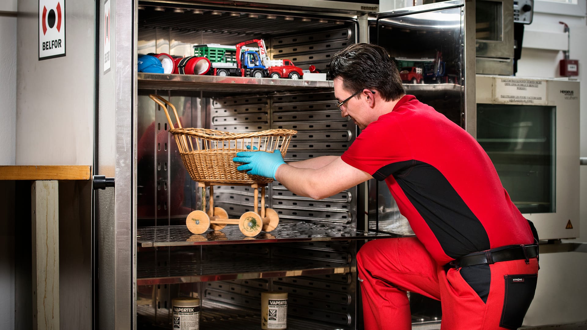 Un ouvrier porte un costume rouge et répare une petite structure en bois.