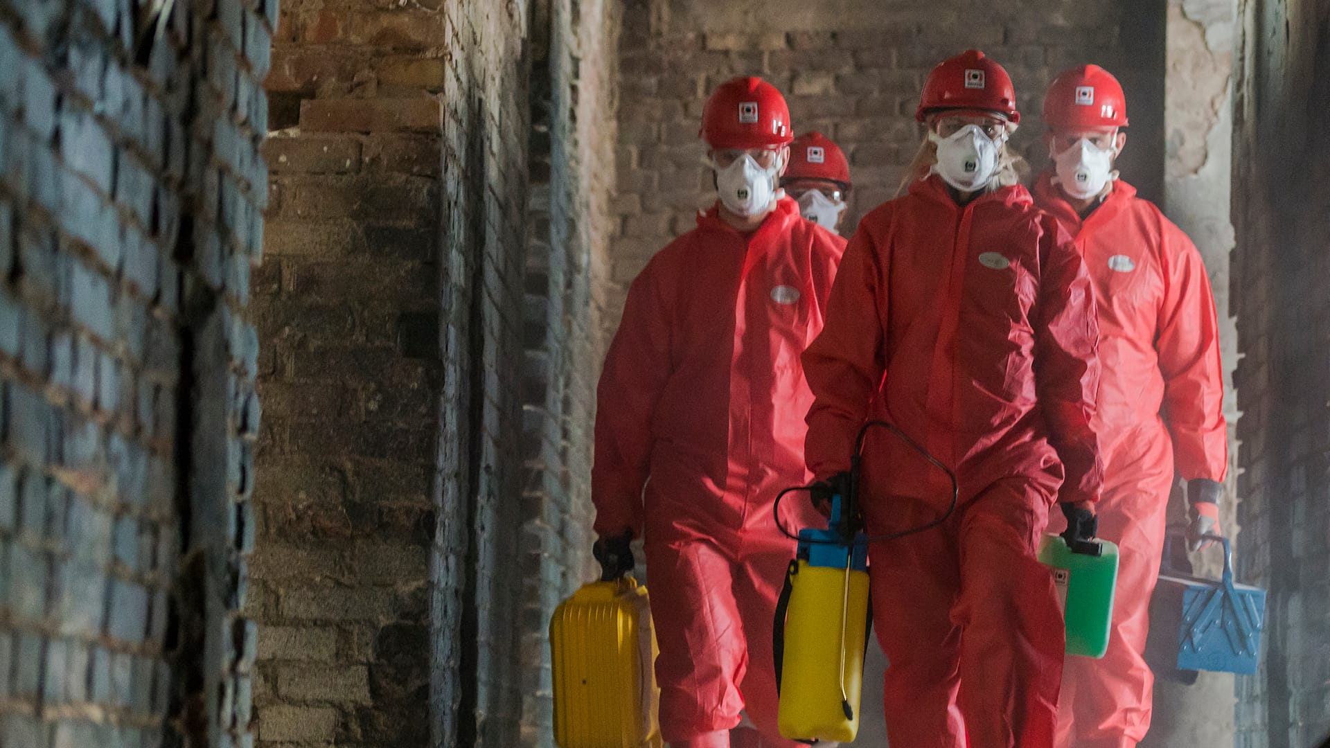 Des travailleurs masculins portant des combinaisons EPI rouges marchent dans la structure endommagée