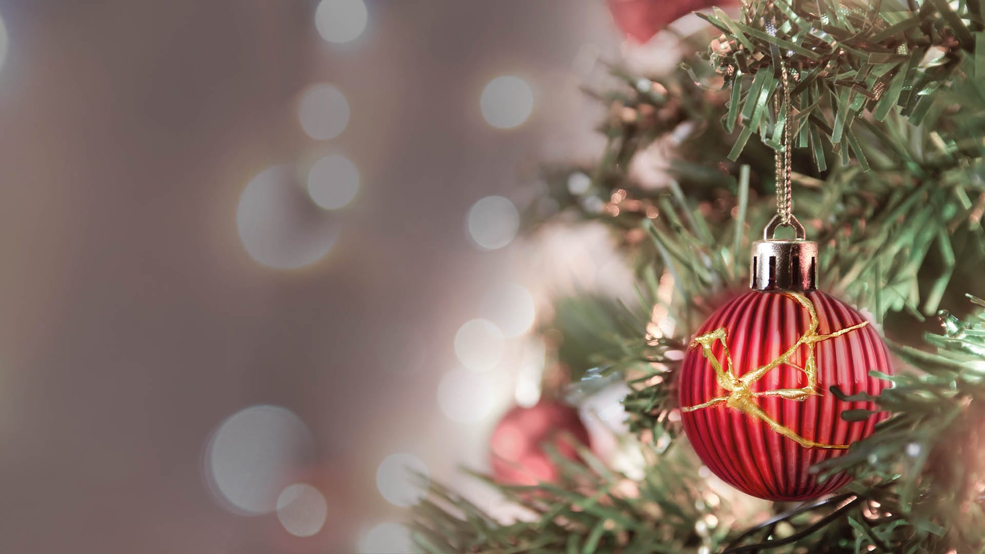 Een rood, geribbeld kerstornament met gouden lijnen hangt aan een groene kerstboom