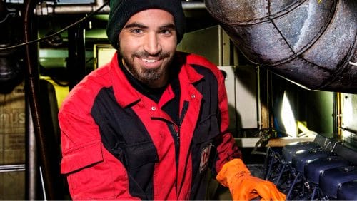 Ein Mann in roter Jacke und orangefarbenen Handschuhen lächelt