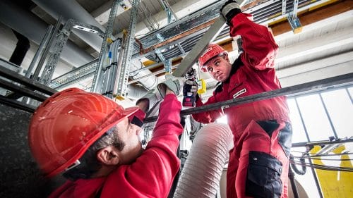 Deux hommes portant un casque de protection rouge travaillent sur un tuyau sur un chantier de construction