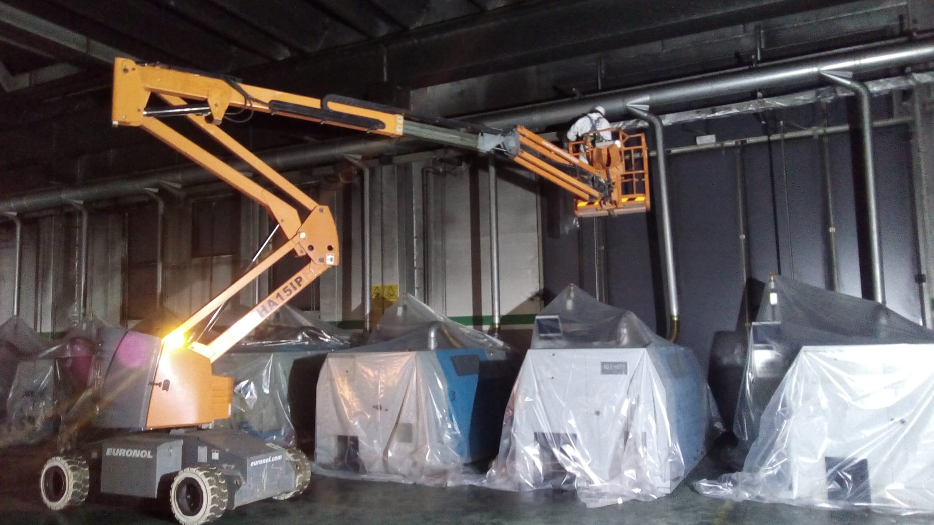 A male employee is fixing a wall while on a lifting equipment