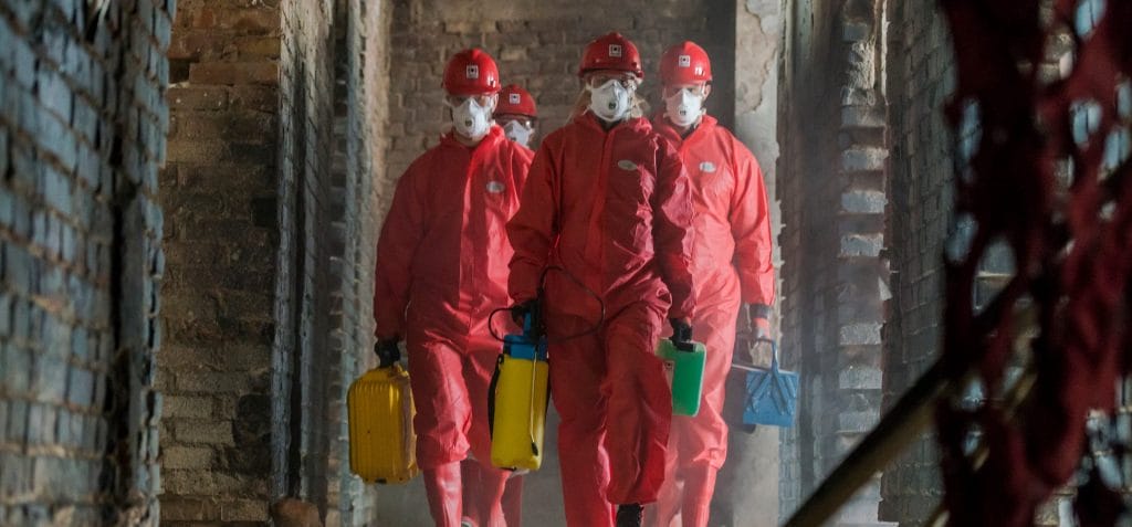 Employees in red PPE suits walking in a damaged structure