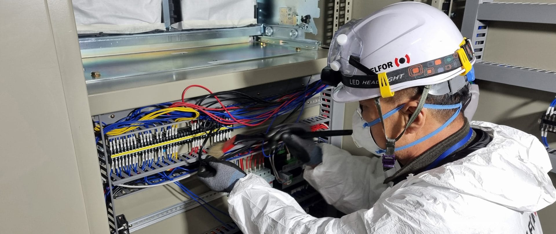 A Male BELFOR employee in PSA working on a switchboard