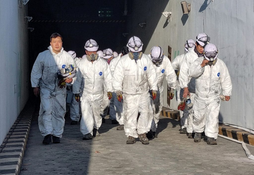 A group of blue collar worker walking out of a tunnel