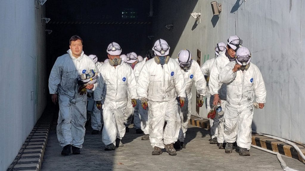 A group of blue collar worker walking out of a tunnel