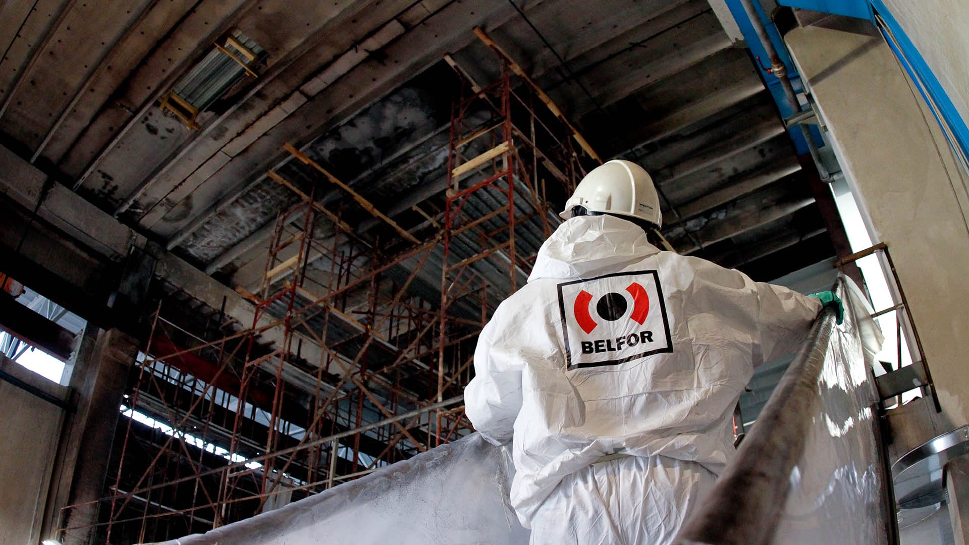 Male employees in red PPE suits walking in a damaged structure