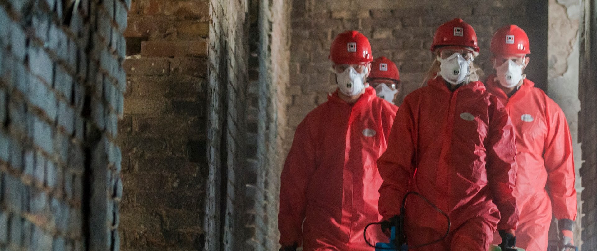 Male employees in red PPE suits walking in a damaged structure