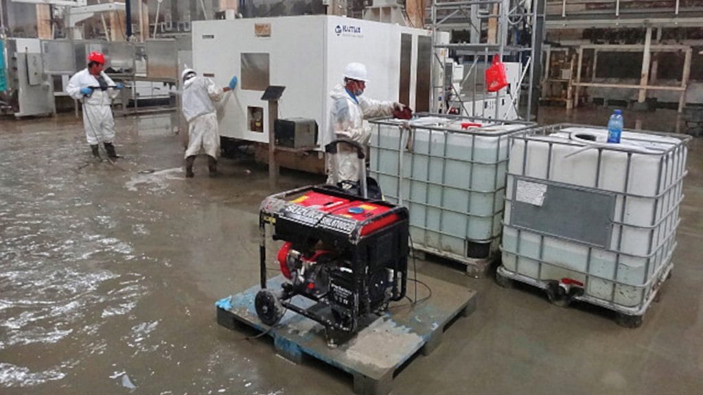 Workers PPE address water damage in an industrial facility, with a generator and large water containers