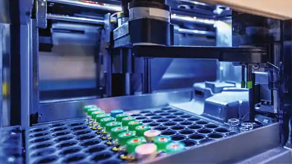 Automated laboratory equipment processing multiple vials with green caps in a high-tech, blue-lit environment