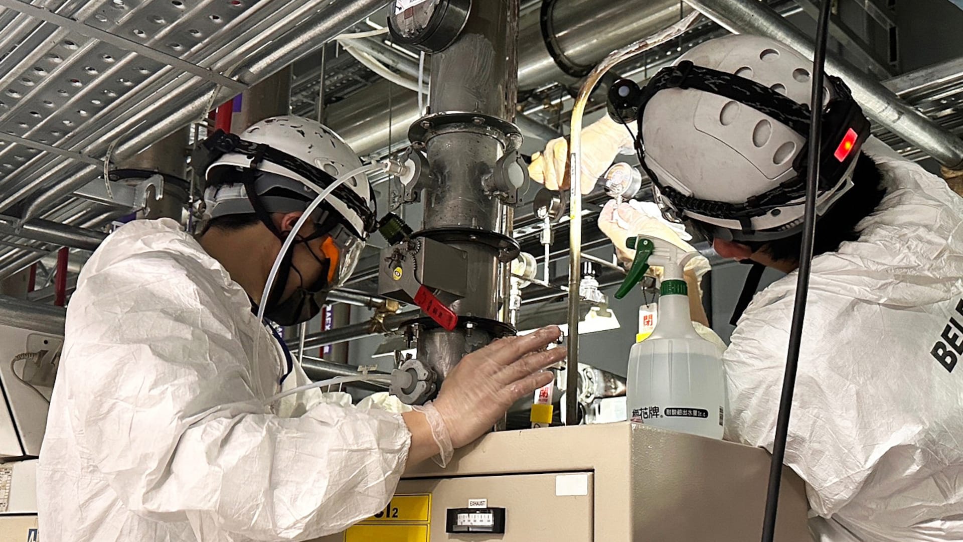 Two BELFOR technicians in protective suits and helmets work on an industrial plant and inspect a pipeline