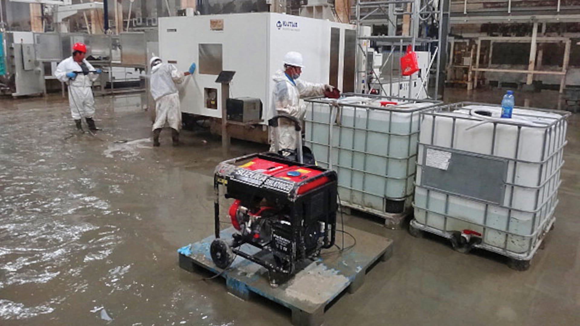 Workers PPE address water damage in an industrial facility, with a generator and large water containers