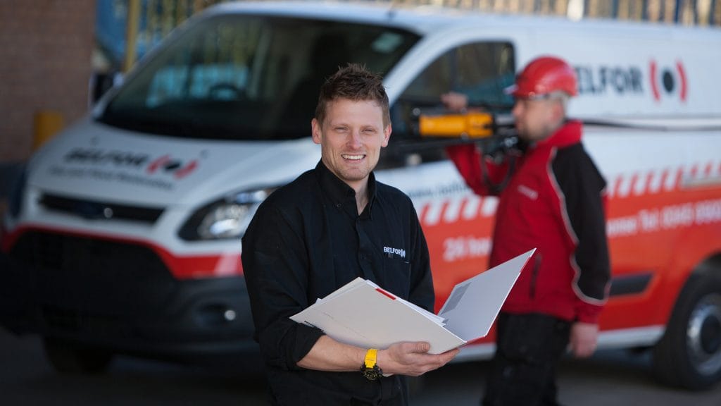 A BELFOR project manager holding a paper folder in front of a van